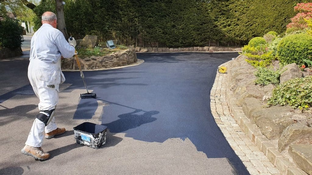 man painting a tarmac driveway with a paint roller